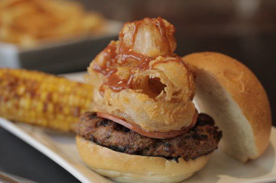 Rodeo Burger: A BBQ Pork Burger topped with Buffalo Fried Onion Rings, Canadian Bacon and Drizzled with Hickory Smoked Steak Sause, served with Deep Fried Corn on the Cob.